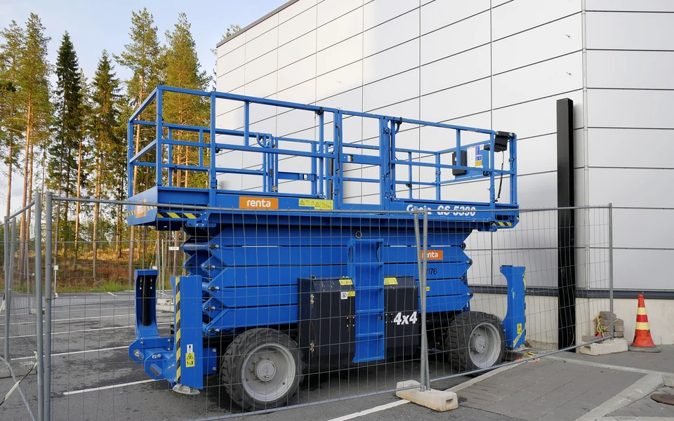 A rough terrain scissor lift beside an industrial building.